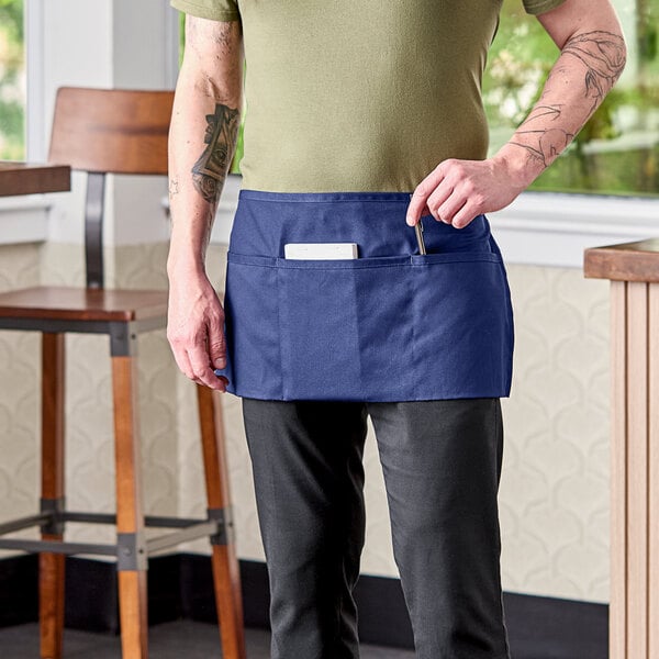 A man wearing a navy blue Uncommon Chef waist apron with three pockets standing in a kitchen.