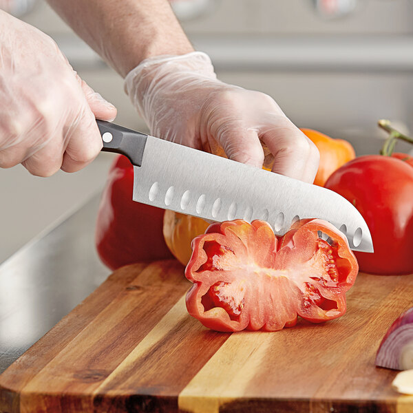 A person in gloves using a Wusthof Gourmet Santoku knife to cut a tomato.