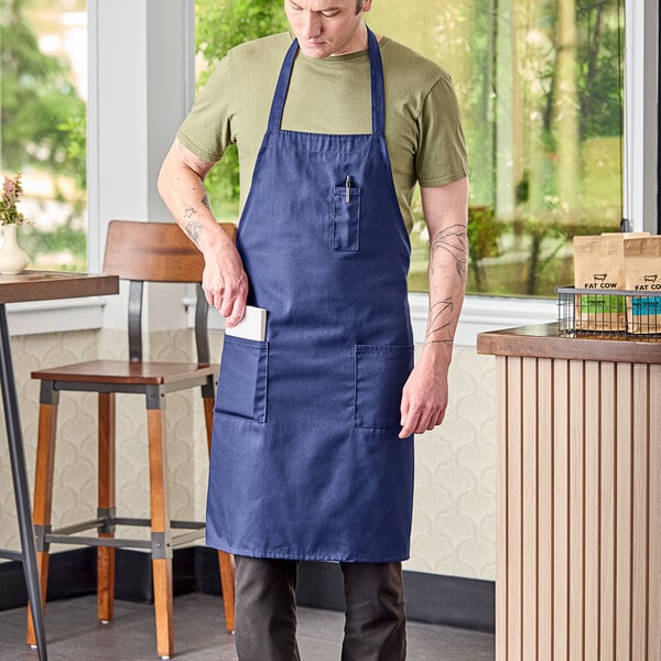 A man wearing a navy blue Uncommon Chef bib apron with three pockets.