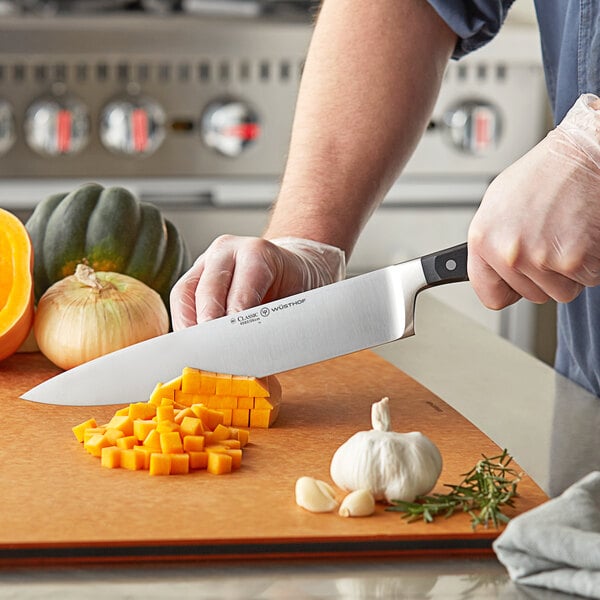 A person using a Wusthof Classic Cook's Knife to cut green pumpkin and yellow onion on a counter.