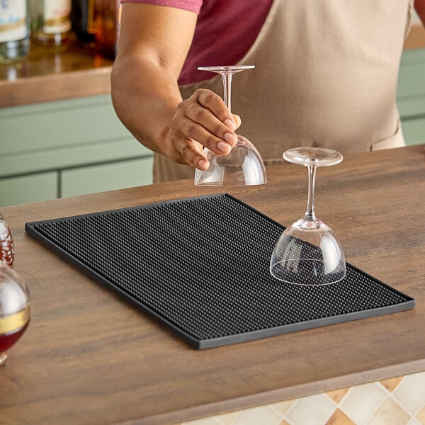 A man pouring wine onto an American Metalcraft black rubber bar mat on a bar counter.
