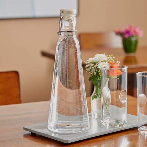 An American Metalcraft clear acrylic hinged water bottle on a table with glasses and a clear liquid.