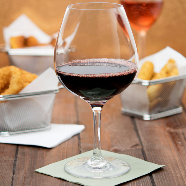 A Carlisle plastic balloon wine glass filled with red wine on a table.