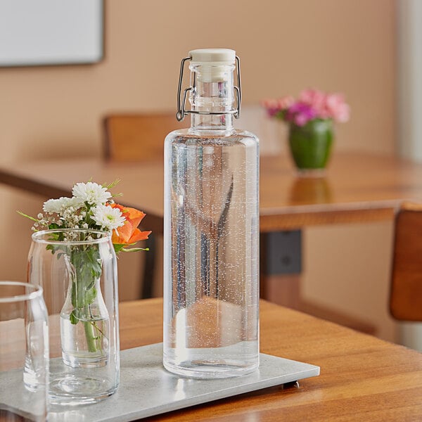 An American Metalcraft clear acrylic hinged water bottle with a glass of water on a table.