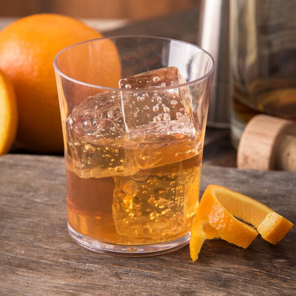 A Carlisle plastic rocks glass filled with liquid, ice, and a slice of orange.