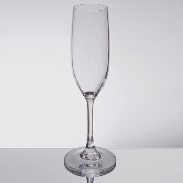 A clear Carlisle plastic champagne flute with a stem on a table.