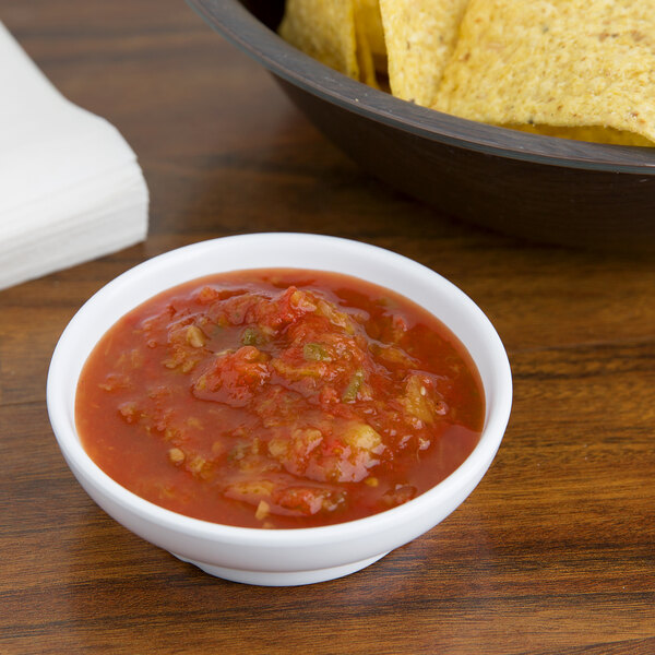 A white GET salsa dish filled with salsa next to a bowl of tortilla chips on a table.