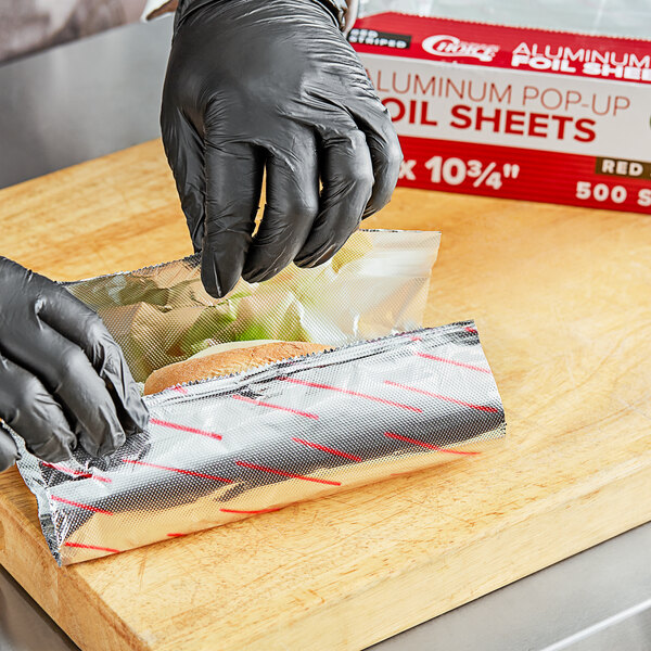 A person in black gloves wrapping a sandwich in red striped foil.