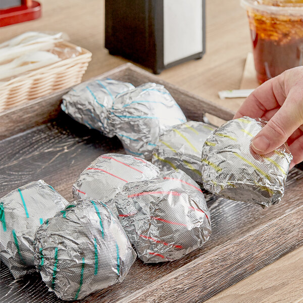 A hand holding a foil wrapper with foil wrapped food inside.