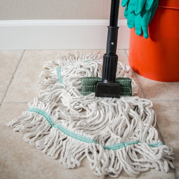 A Carlisle wet mop head with a green headband on the floor next to a mop bucket.