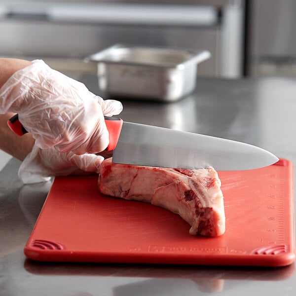 A person using a Dexter-Russell chef knife to cut meat on a red cutting board.