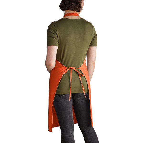 A woman wearing an orange Intedge bib apron with 2 pockets.