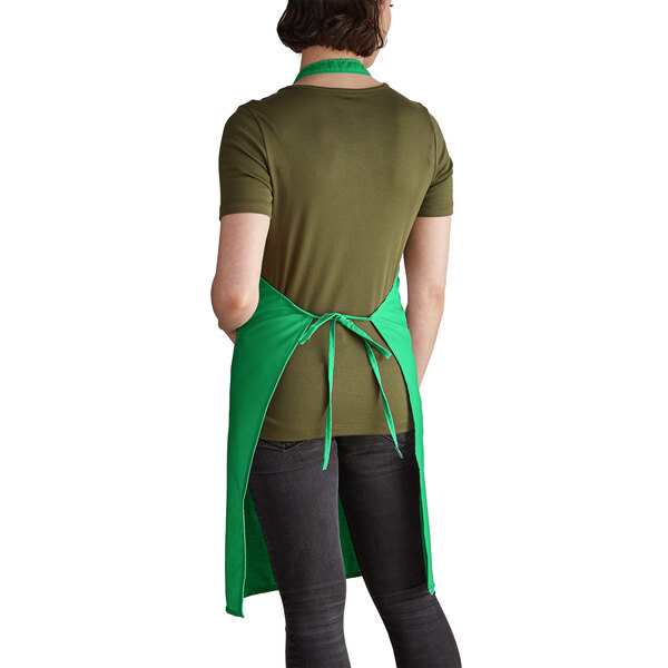 A woman wearing a green Intedge bib apron with pockets standing in a professional kitchen.