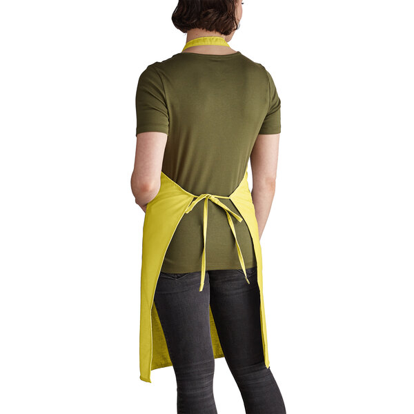 A woman wearing a yellow Intedge bib apron with two pockets standing in a professional kitchen.