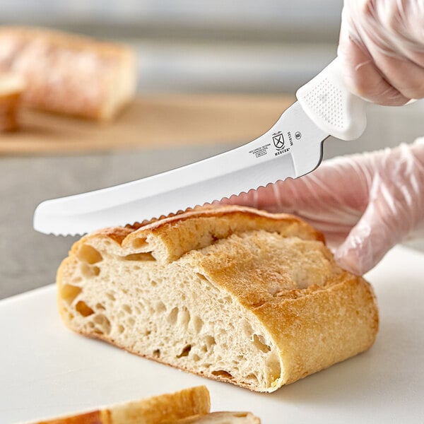 A person using a Mercer Culinary bread knife to cut bread on a cutting board.