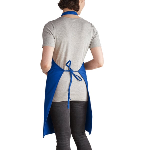 A woman wearing a royal blue Intedge bib apron with 2 pockets.