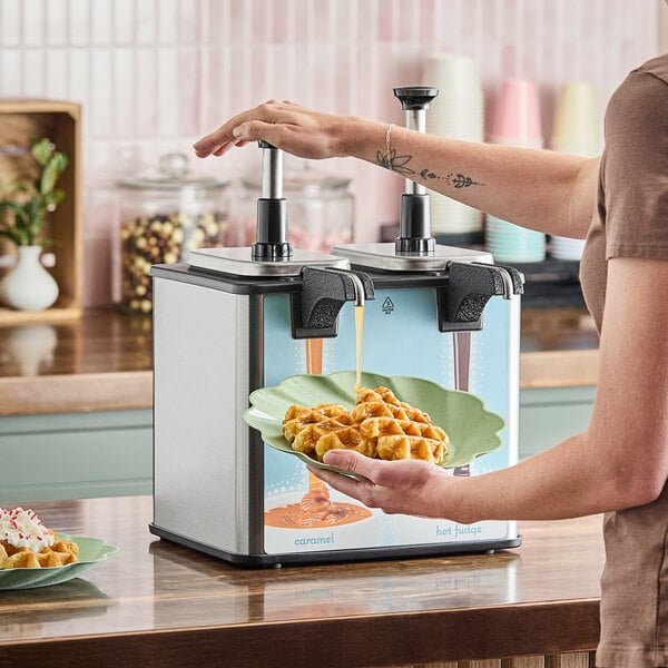 A twin topping warmer with heated spouts being used to dispense caramel sauce onto waffles.