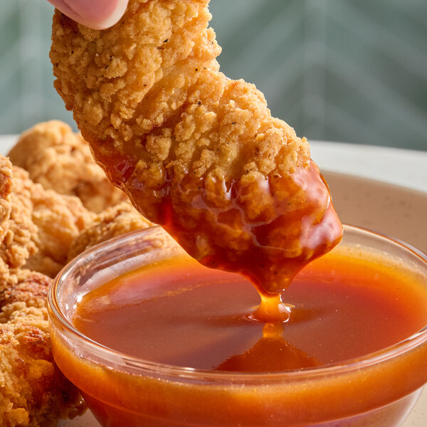 A breaded chicken tender being dipped into a bowl of TABASCO Sweet Chili Hot Sauce.