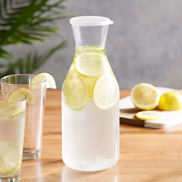 A Choice polycarbonate carafe with lemons and a glass of water on a table.