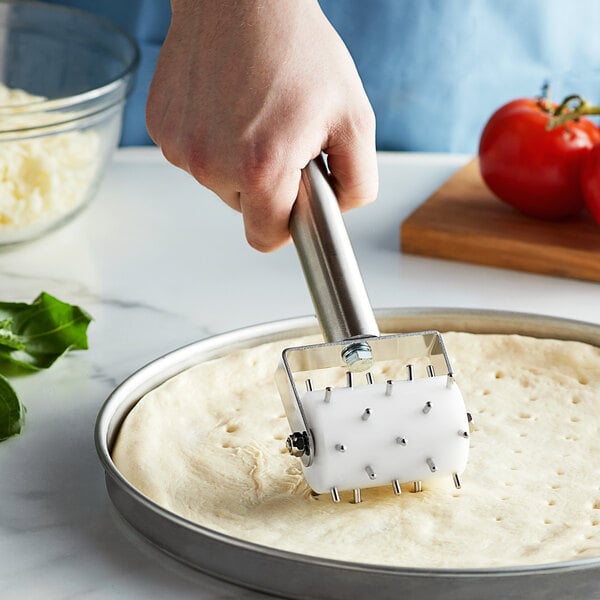 A hand holding an American Metalcraft dough docker with a metal tube and metal handle.