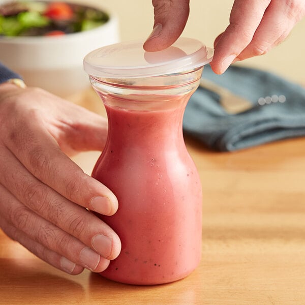 A hand holding a Choice polycarbonate carafe of pink liquid with a plastic lid