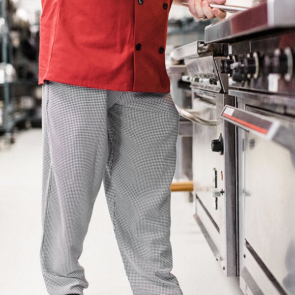 A man in Uncommon Chef houndstooth chef pants and a red jacket standing in a kitchen.