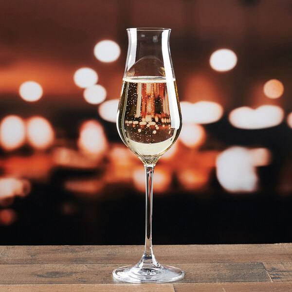 A clear 8 oz. sparkling champagne flute glass filled with champagne, set on a wooden surface with a blurred background.