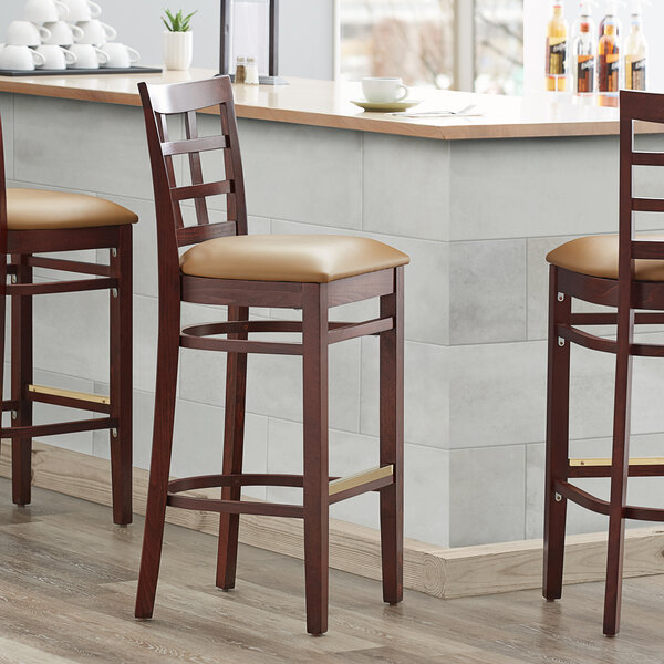 Three Lancaster Table & Seating mahogany wood bar stools with light brown vinyl window backs and seats at a bar counter.