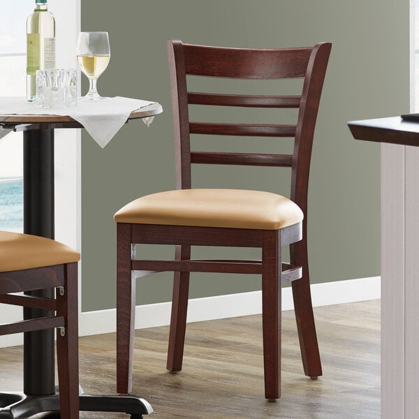 A pair of Lancaster Table & Seating Mahogany wood chairs with light brown vinyl seats next to a table.