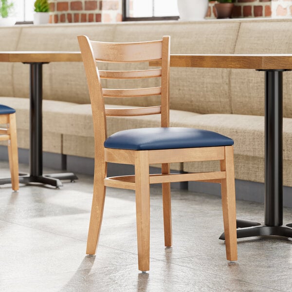 A Lancaster Table & Seating wooden chair with a navy vinyl cushion at a table in a restaurant.