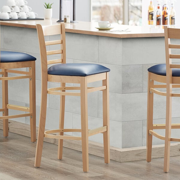 Three Lancaster Table & Seating wooden bar stools with navy vinyl seats at a counter.