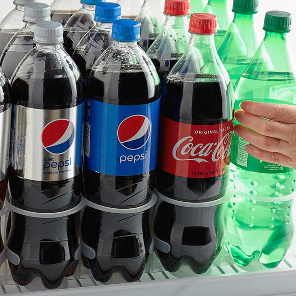 A hand holding a 32 oz. bottle of soda in a refrigerator.