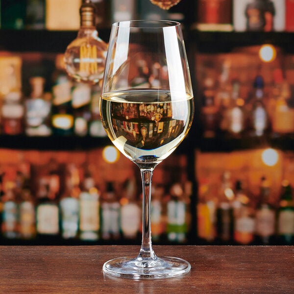A clear Lucaris Temptation 12.5 oz. Chardonnay wine glass filled with white wine, placed on a wooden surface.