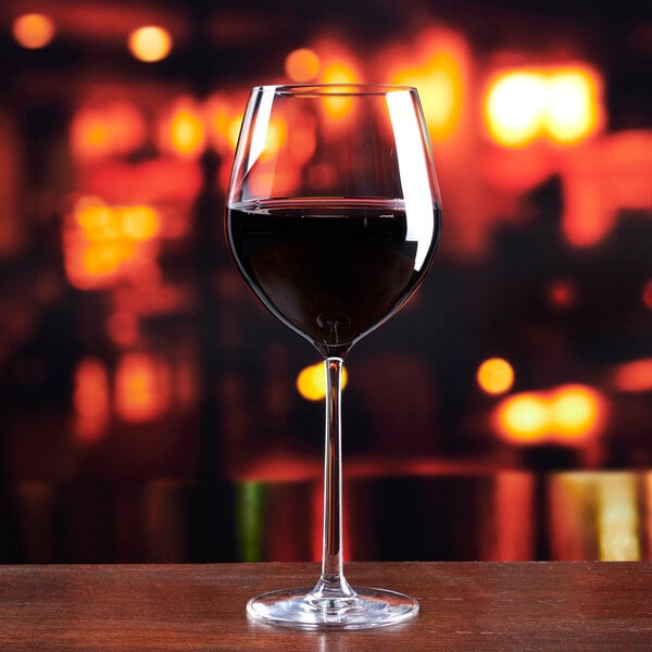 A clear Lucaris Soul 22.5 oz. Burgundy wine glass filled with red wine, set against a blurred warm-toned background.