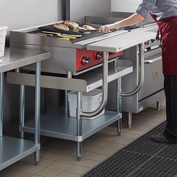 A woman in a red apron using a Regency stainless steel equipment stand to cook food on a grill.