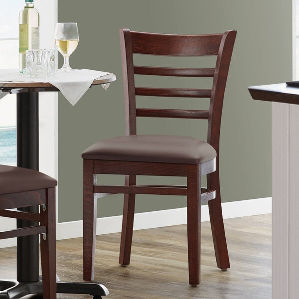 A Lancaster Table & Seating mahogany wood chair with a dark brown vinyl seat next to a table.