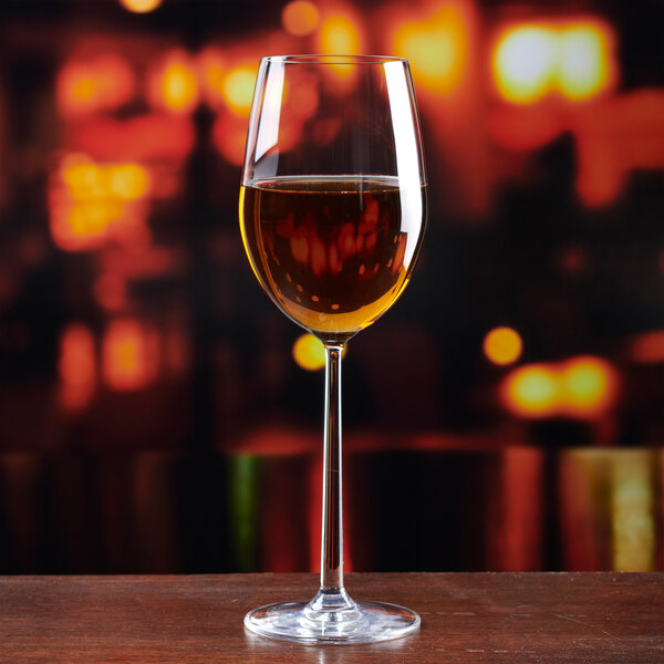 A clear Lucaris Soul from Anchor Hocking Foodservice 14 oz. Chardonnay wine glass filled with white wine, set against a blurred warm-toned background.
