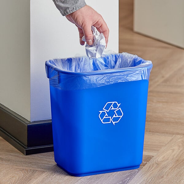 A person putting a plastic bag into a blue Continental Recycling Wastebasket with a recycle symbol on it.
