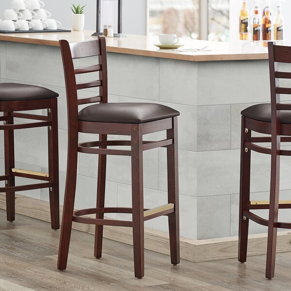 Three Lancaster Table & Seating mahogany wood barstools with dark brown vinyl seats and ladder backs.