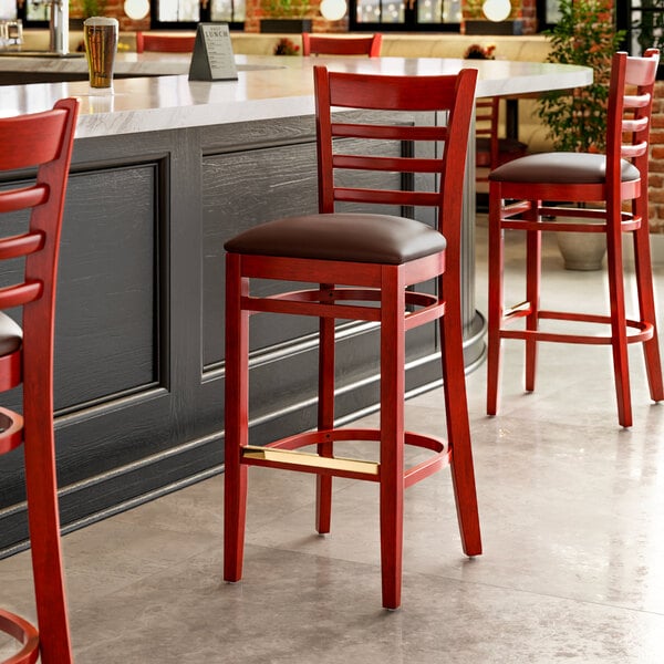 A row of Lancaster Table & Seating mahogany wood bar stools with dark brown vinyl seats in a restaurant.