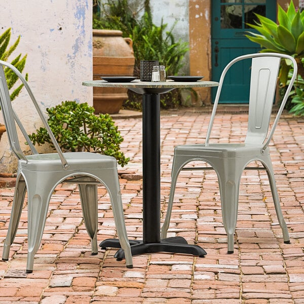 A black table base on a brick patio with two chairs.
