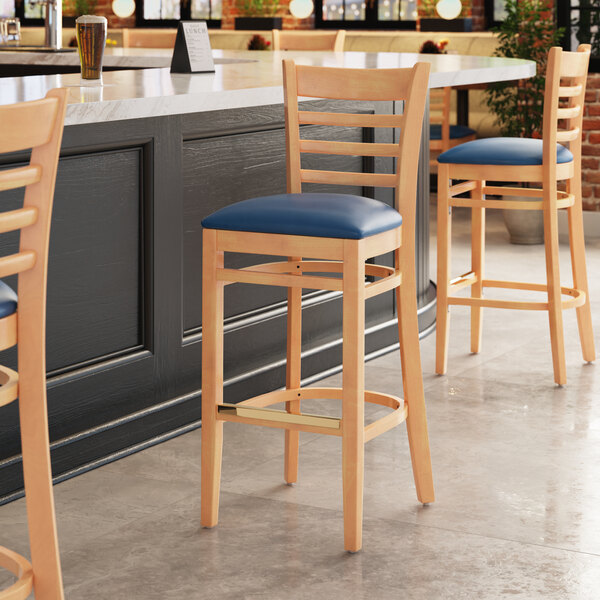 A Lancaster Table & Seating wooden bar stool with a navy vinyl seat.