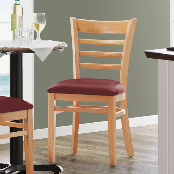 A pair of Lancaster Table & Seating wooden chairs with burgundy vinyl seats at a table in a restaurant.