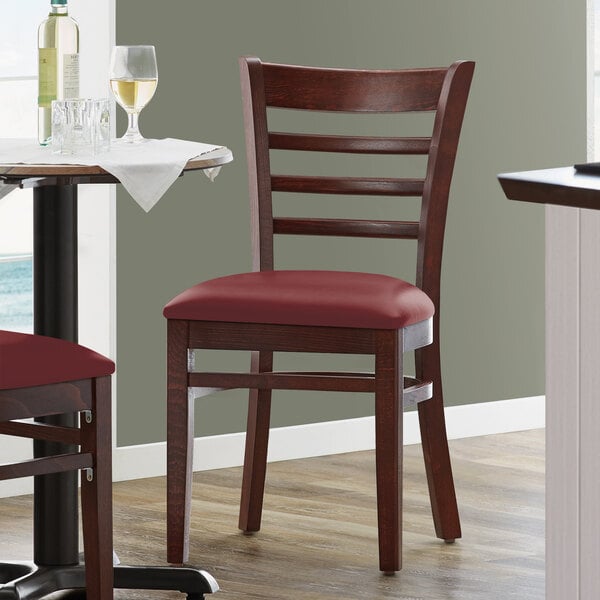 A Lancaster Table & Seating mahogany wood chair with a burgundy vinyl seat next to a table.