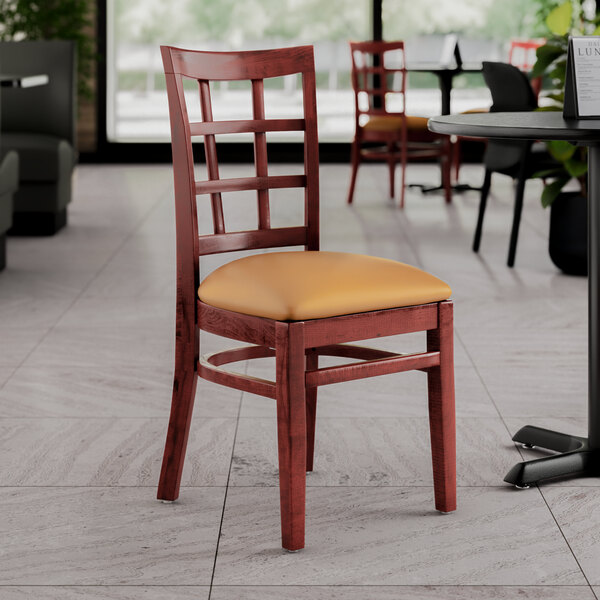 A Lancaster Table & Seating mahogany wood chair with a light brown vinyl seat at a table in a restaurant