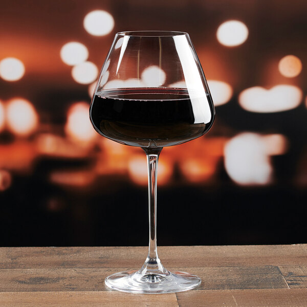 A clear, stemmed red wine glass partially filled with red wine, placed on a wooden surface.