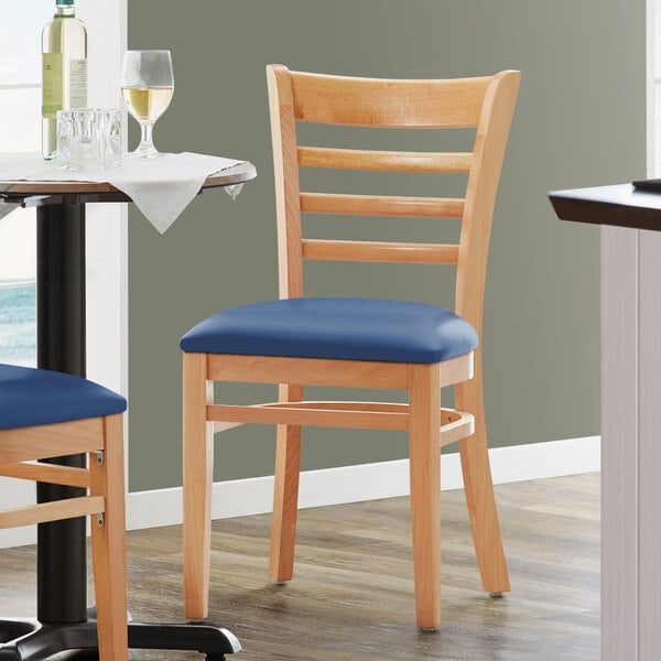 Two Lancaster Table & Seating wood chairs with navy vinyl seats next to a table in a restaurant.