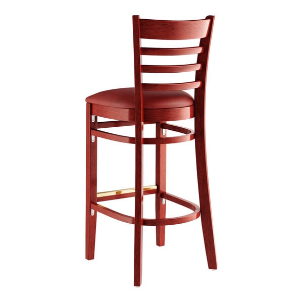 A Lancaster Table & Seating mahogany wood bar stool with a burgundy cushion on the seat.