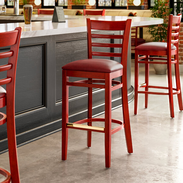A Lancaster Table & Seating mahogany wood bar stool with a red leather seat.
