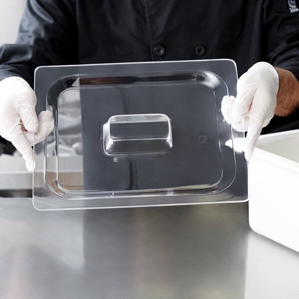 A person in gloves holding a Carlisle clear plastic food pan lid over a clear tray.